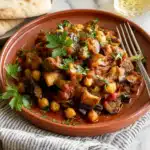 Lebanese eggplant moussaka served on a terracotta plate with chickpeas and herbs, accompanied by warm pita bread on a neutral striped linen.