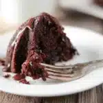 Rich chocolate Bundt cake slice with melted glaze being scooped with a fork on a white plate