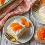 Overhead view of orange creamsicle poke cake squares on plates with mandarin orange segments and vintage forks on rustic wooden background