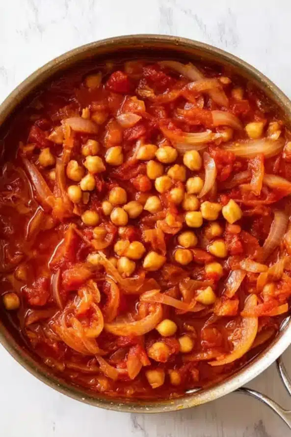  A pan filled with raw sliced onions and whole garlic cloves, ready to be sautéed in olive oil.