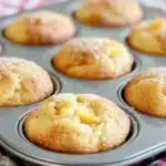 Baked peach cobbler muffins in tin with golden tops and visible peach chunks throughout