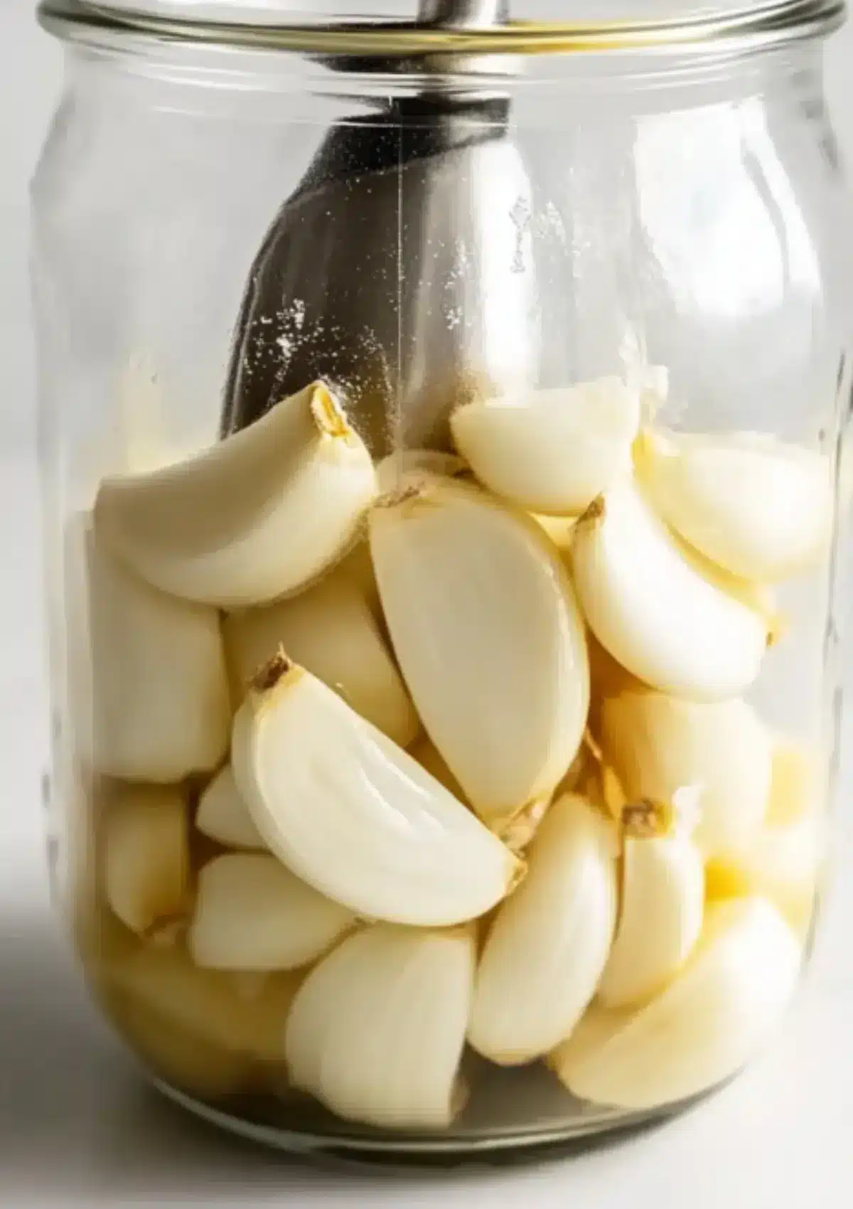 Peeled garlic cloves inside a glass jar with immersion blender ready for blending