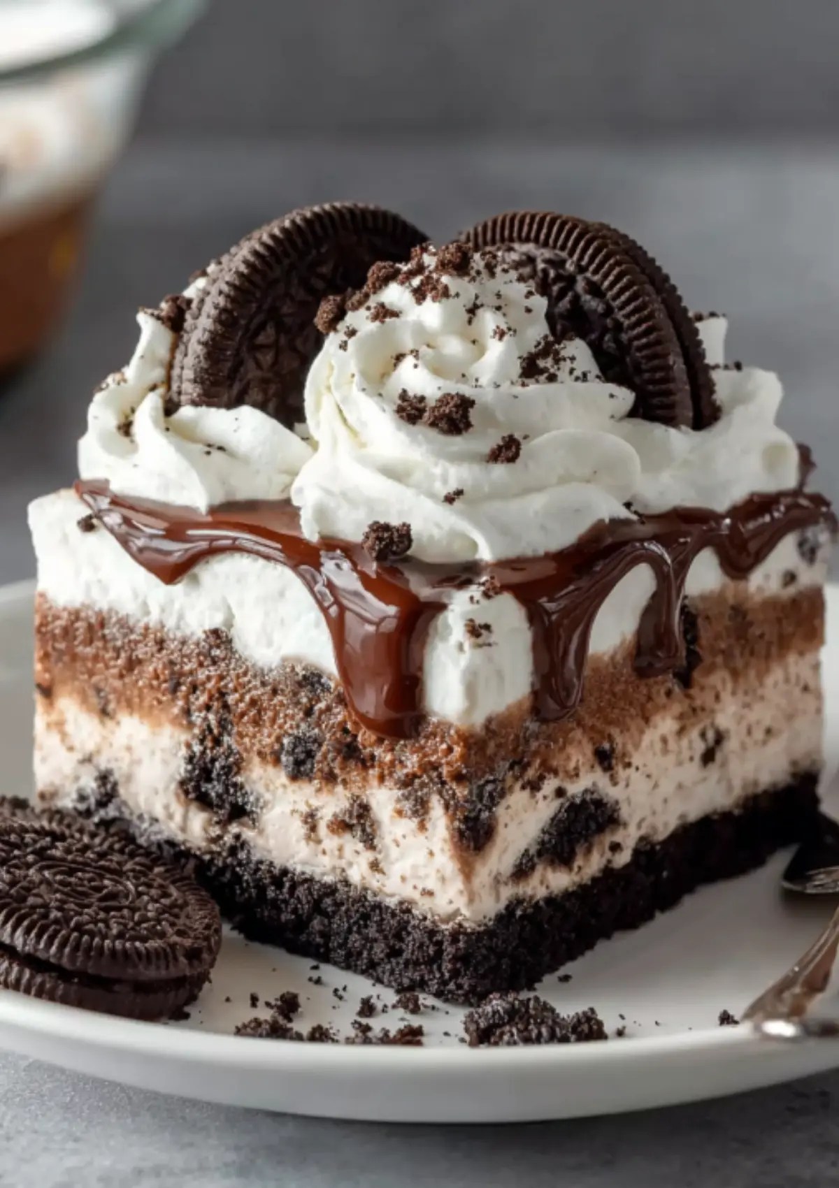 Side view of tall Oreo ice cream cake slice with prominent chocolate drip effect and Oreo cookie garnishes on whipped cream topping