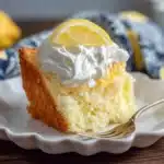 Delicious lemon angel food cake slice topped with fluffy whipped cream and fresh lemon wheel on decorative white plate