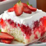 Slice of strawberry cake with white frosting topped with fresh strawberry slices on a white plate with fork