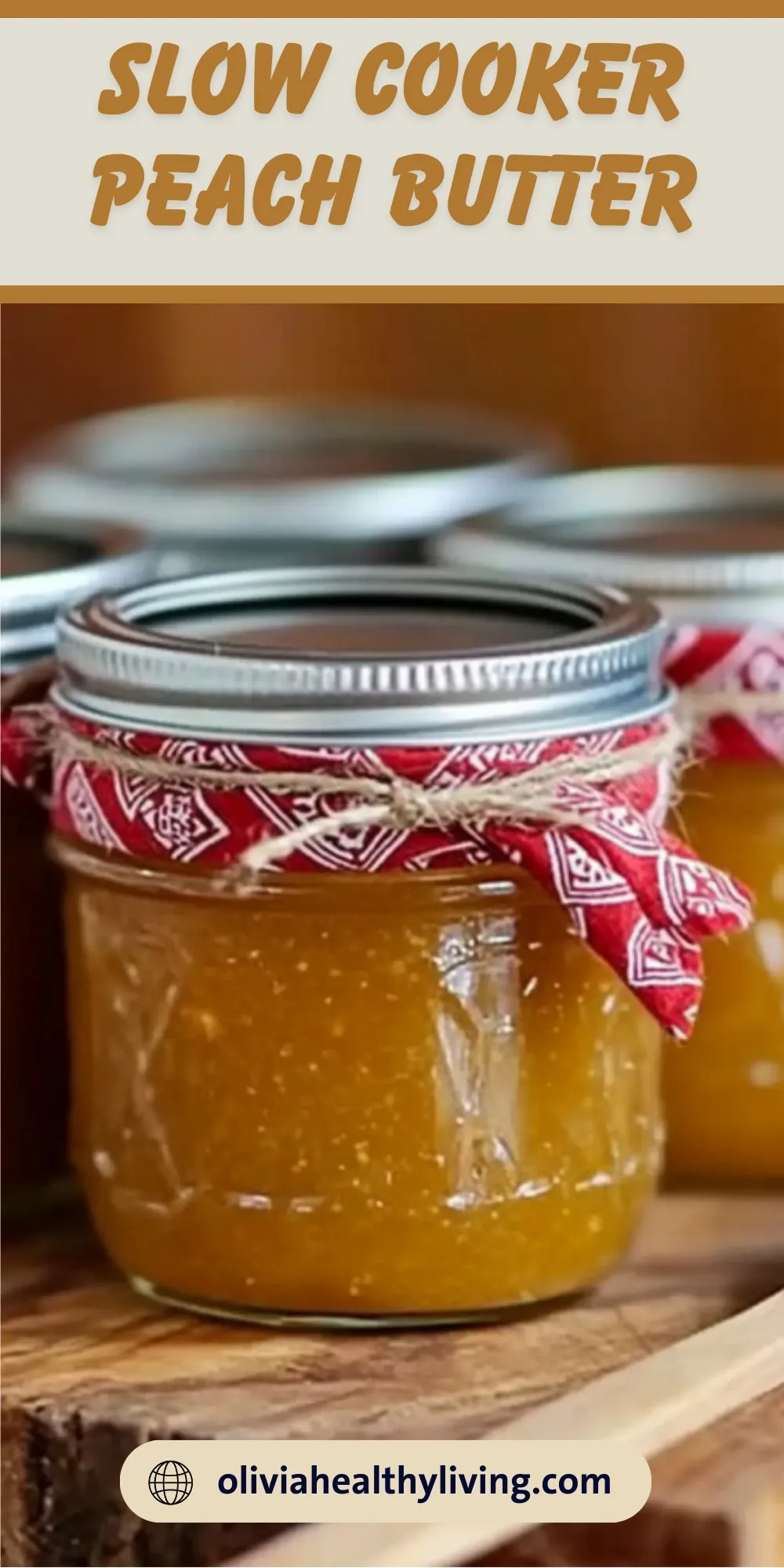 Glass jar of golden homemade peach butter with red bandana ribbon, surrounded by more jars on wooden surface