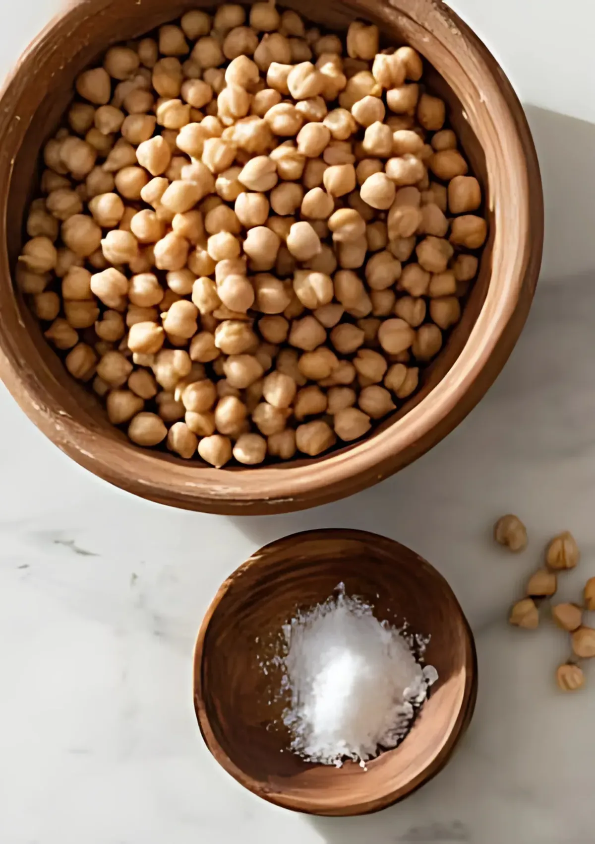 Bowl of soaked chickpeas next to a small bowl of salt on marble surface