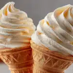 Two vanilla soft serve ice cream cones with vanilla bean specks side by side