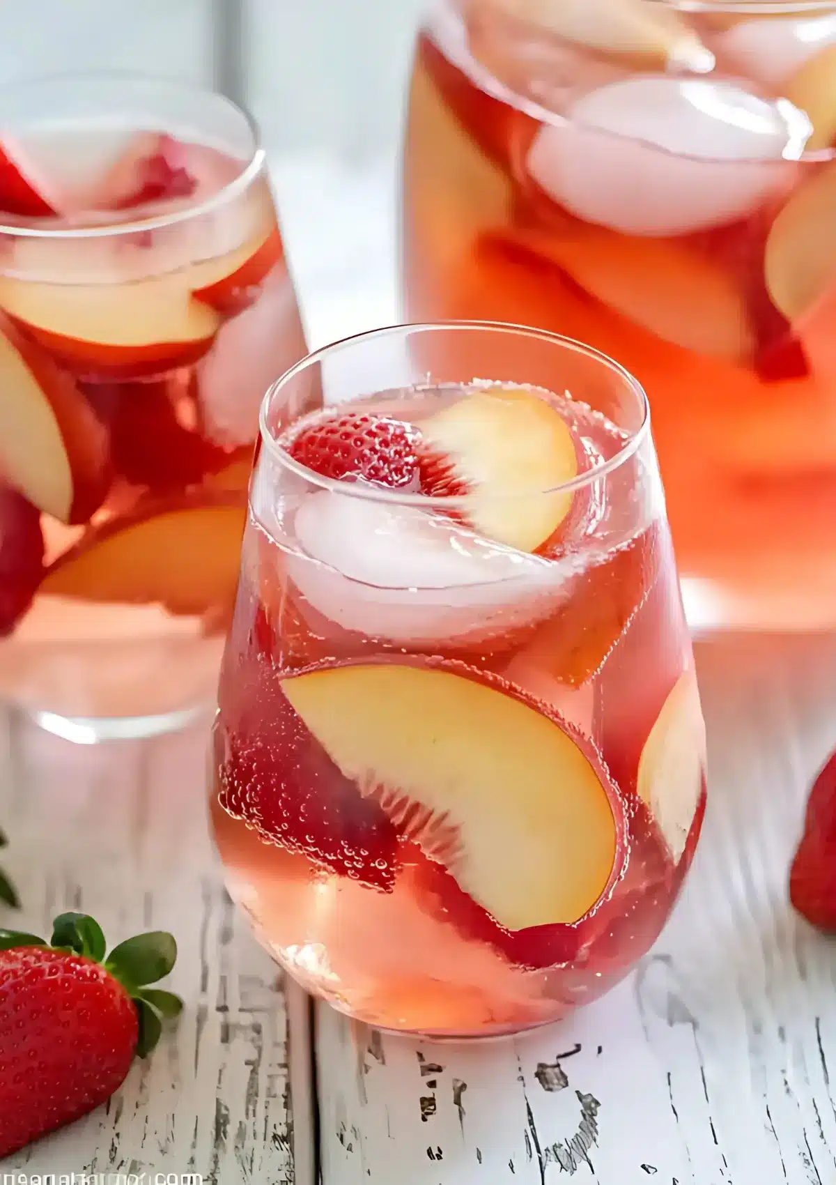 Close-up of peach sangria in wine glass with peach slices and strawberries, multiple glasses in background
