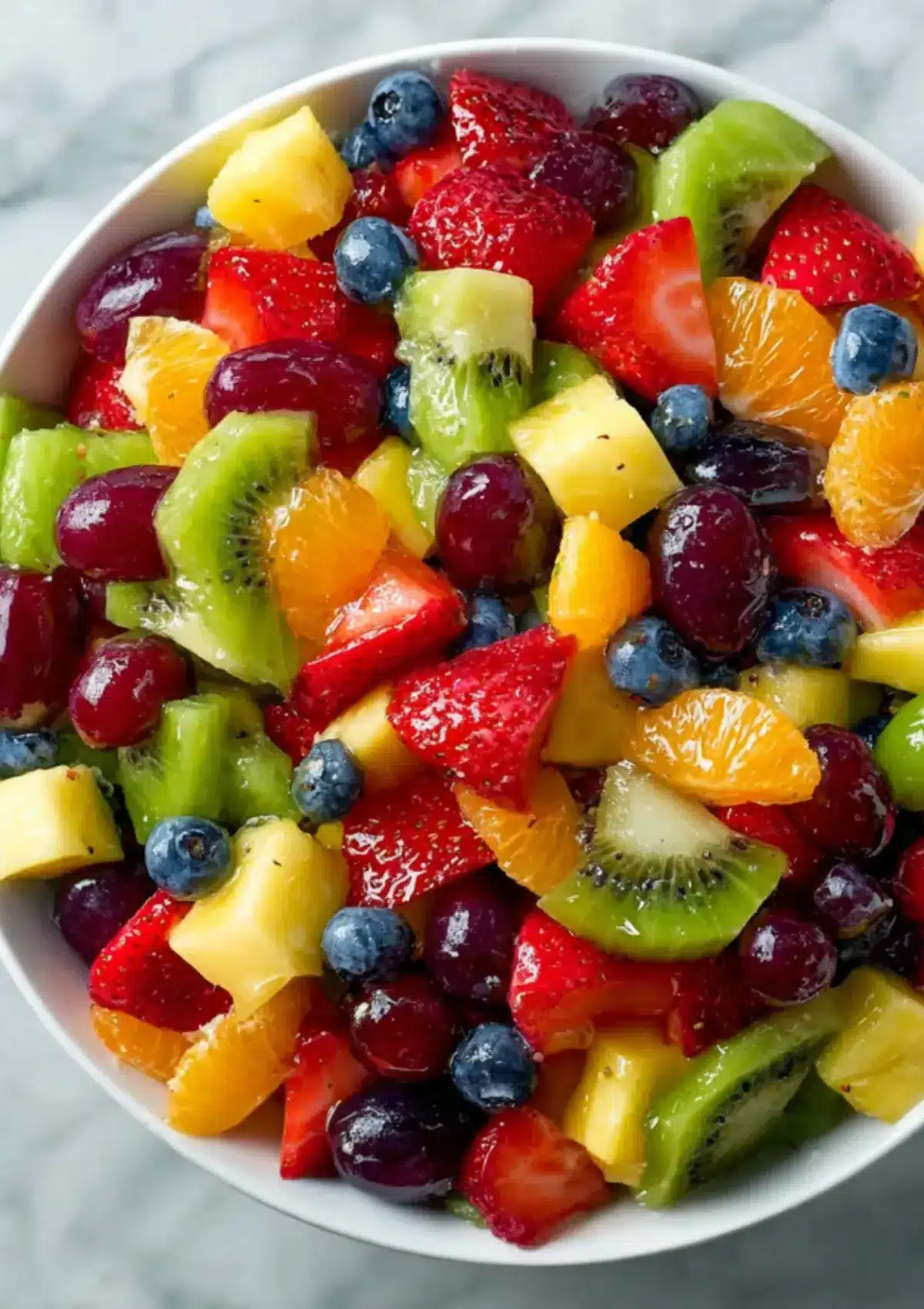 Vibrant rainbow fruit salad in white bowl containing fresh strawberries, pineapple, kiwi, mandarin oranges, red grapes, and blueberries coated in honey lime dressing, showing beautiful color variety and glossy appearance
Réessayer