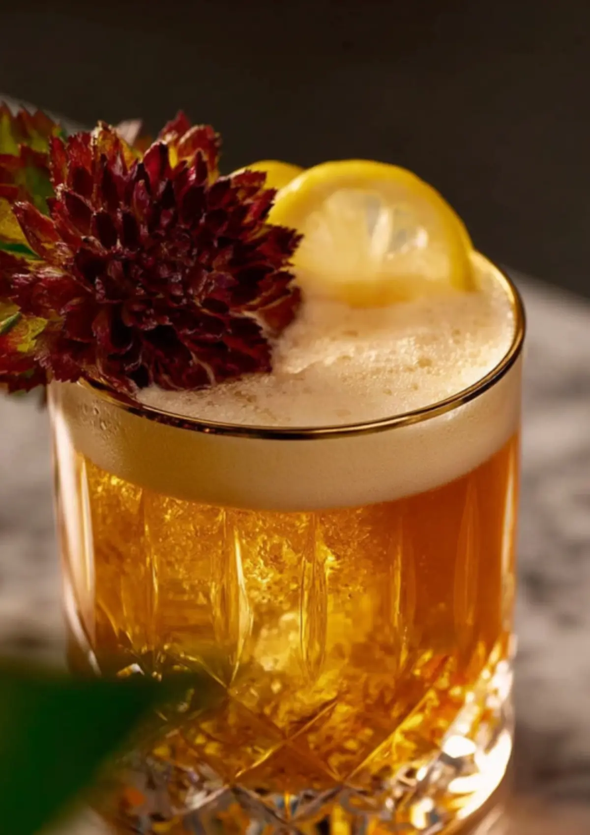 Close-up detail shot focusing on the cocktail's creamy foam top and floral garnish