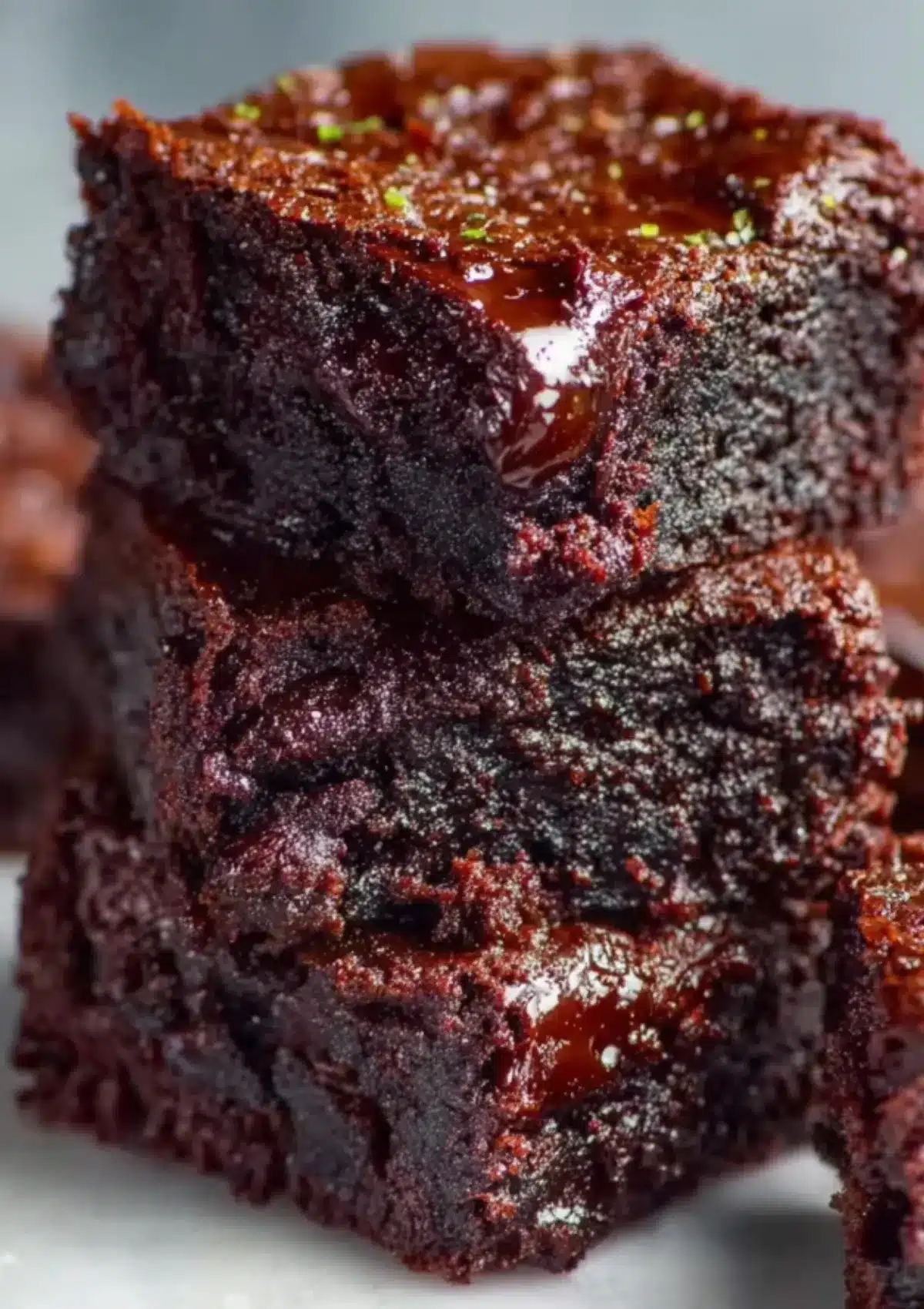Close-up stack of two zucchini brownie squares showing incredibly moist, fudgy interior texture with glossy chocolate surface and lime zest garnish