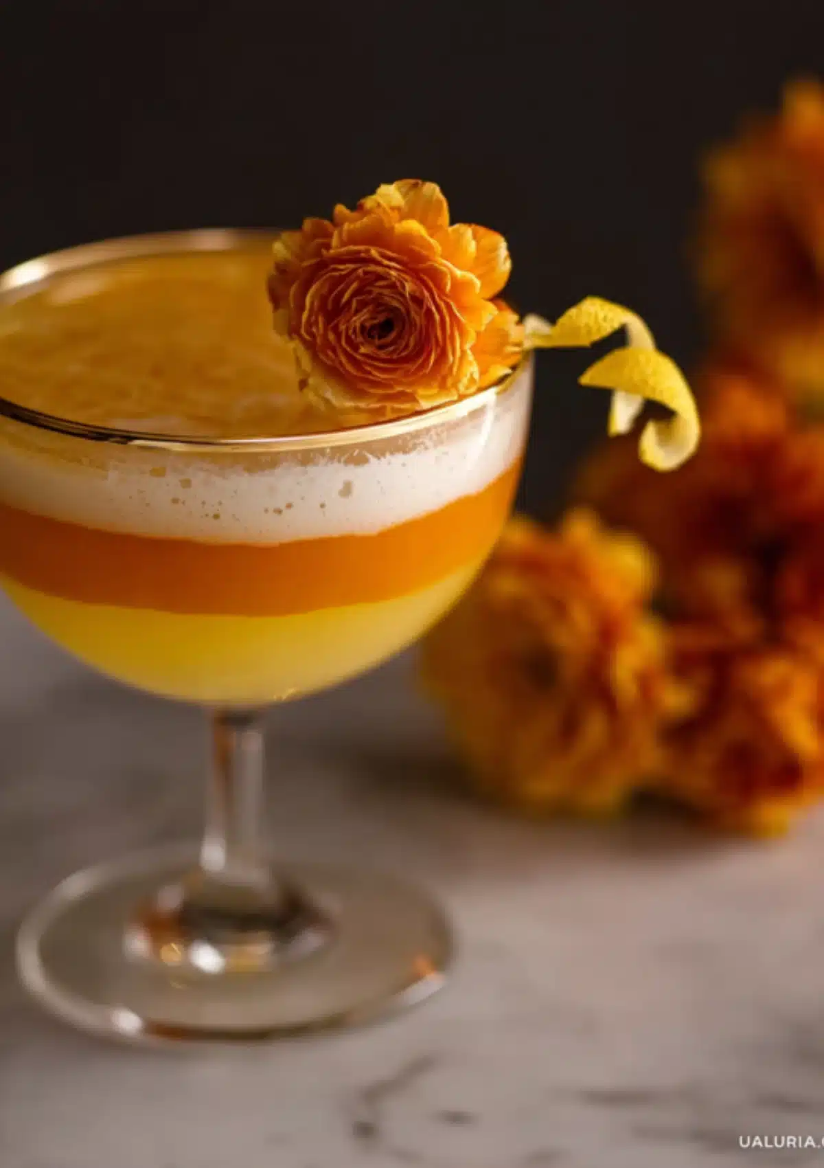 Close up of candy corn cocktail showing distinct orange and yellow layers with ranunculus garnish
