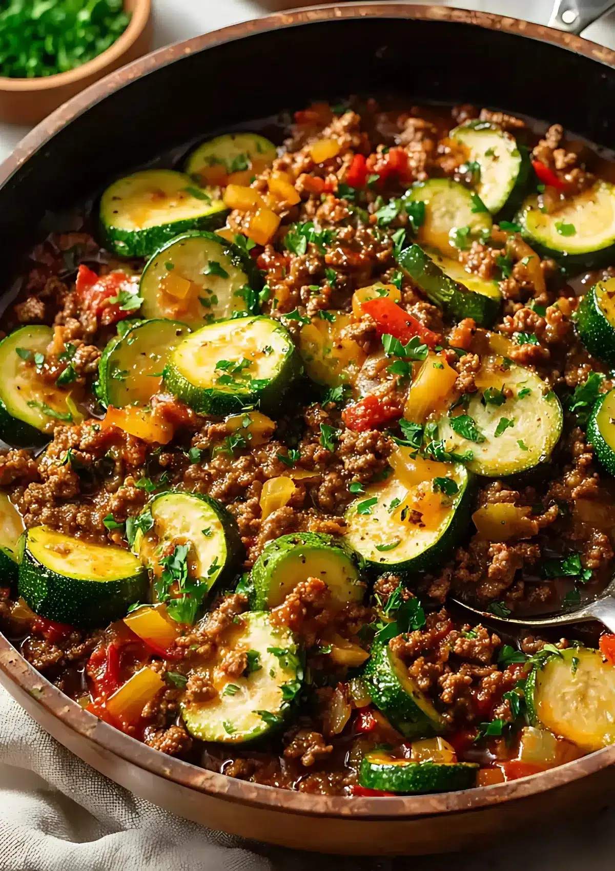 Rustic skillet filled with sautéed zucchini, browned ground beef, bell peppers, and onions in a rich tomato sauce, topped with fresh parsley.