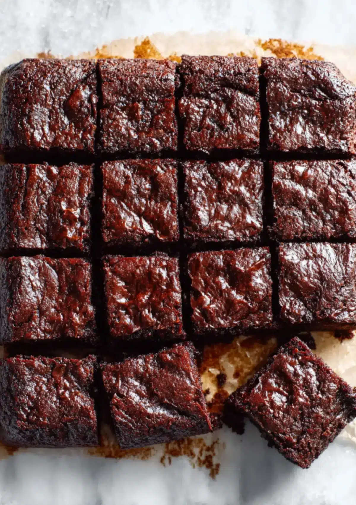 Raw zucchini brownie batter spread evenly in glass baking dish lined with parchment paper, ready to go into the oven