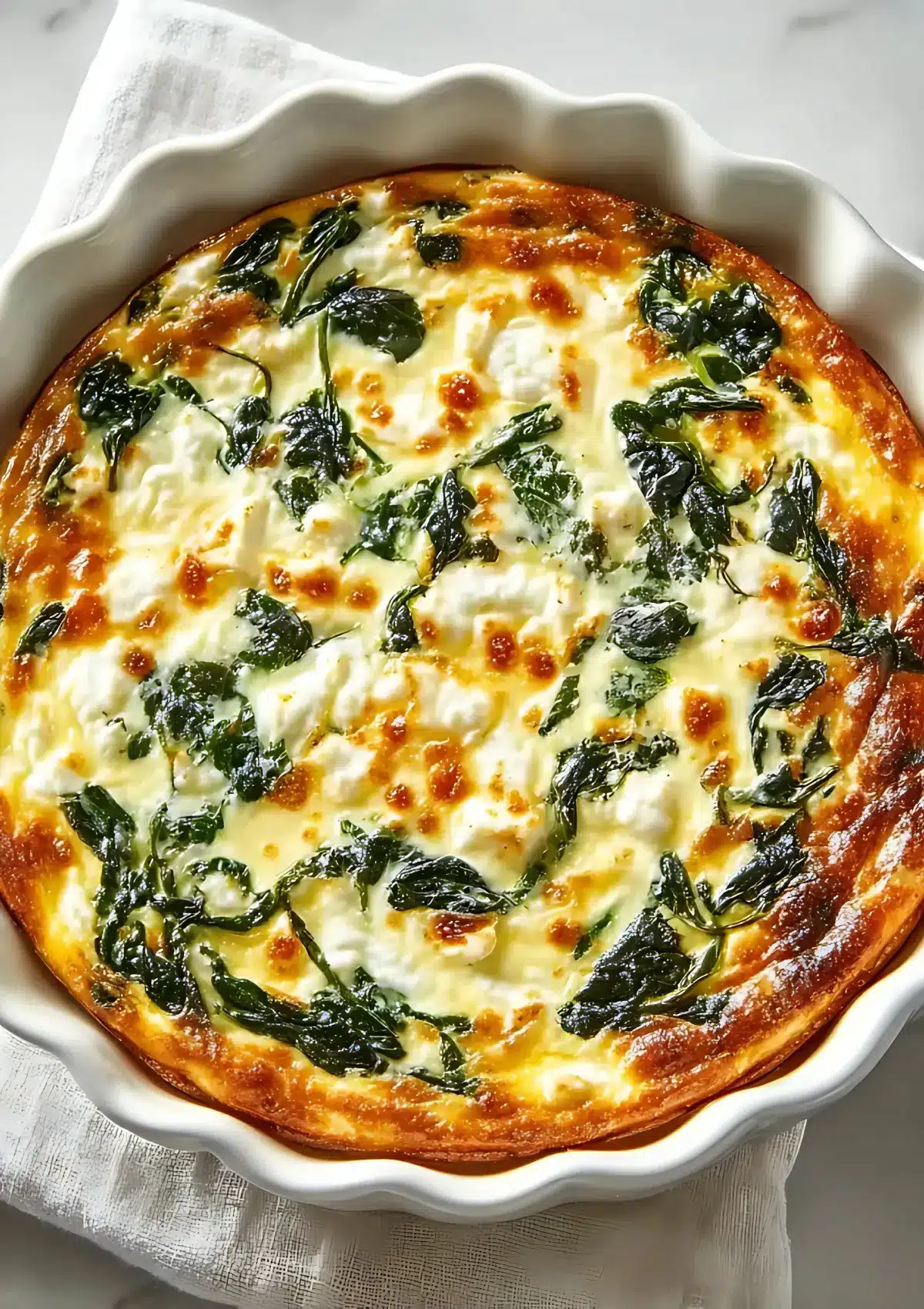 Close-up overhead photo of baked spinach and cottage cheese quiche, showing caramelized edges and creamy melted cheese.