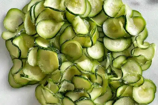 Thin slices of zucchini laid out on a paper towel, slightly curled and glistening with salt-drawn moisture.