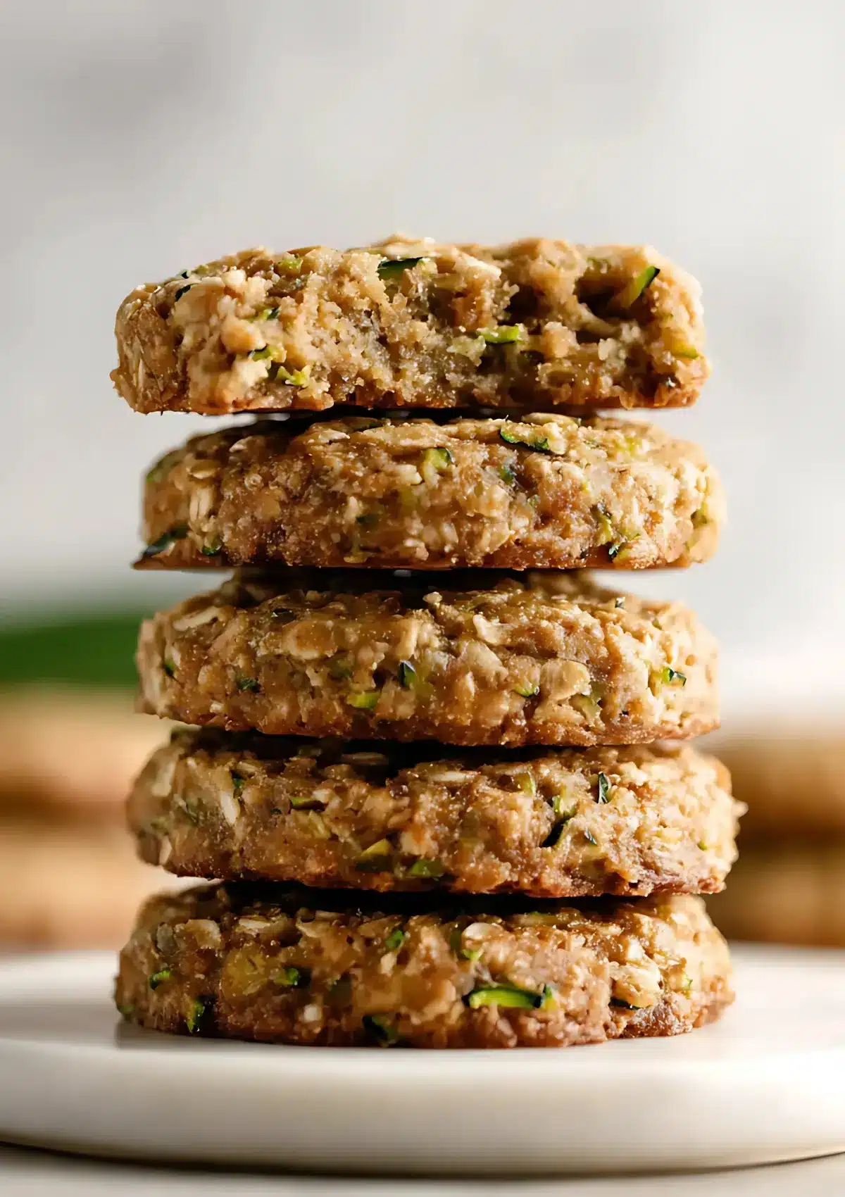 Tall stack of zucchini oatmeal cookies with the top cookie broken open to reveal moist oats and zucchini inside.