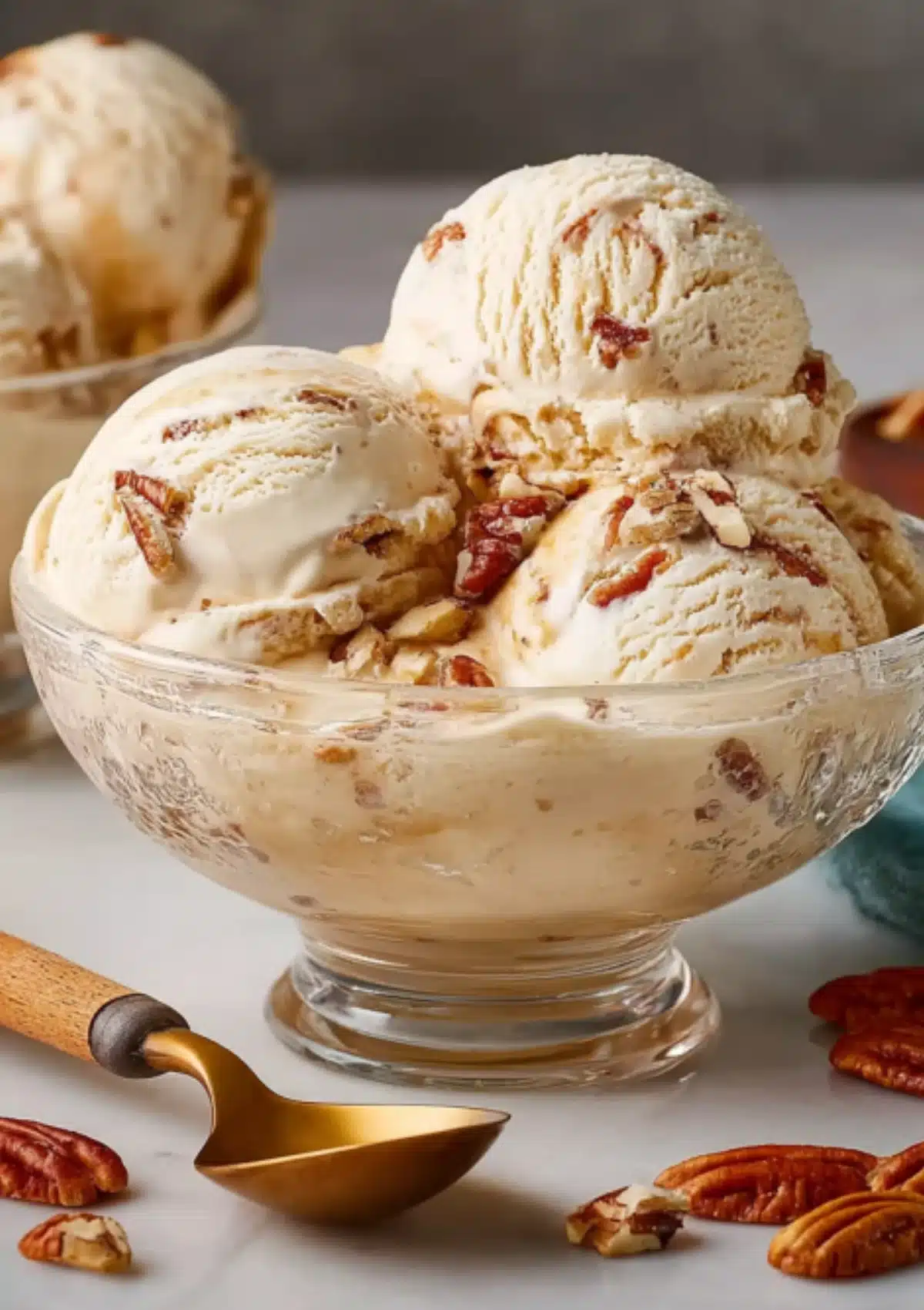 Three scoops butter pecan ice cream in footed glass bowl with vintage ice cream scoop