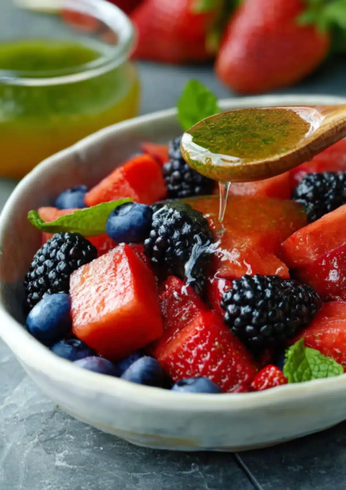 Wooden spoon drizzling honey lime dressing over berry watermelon salad