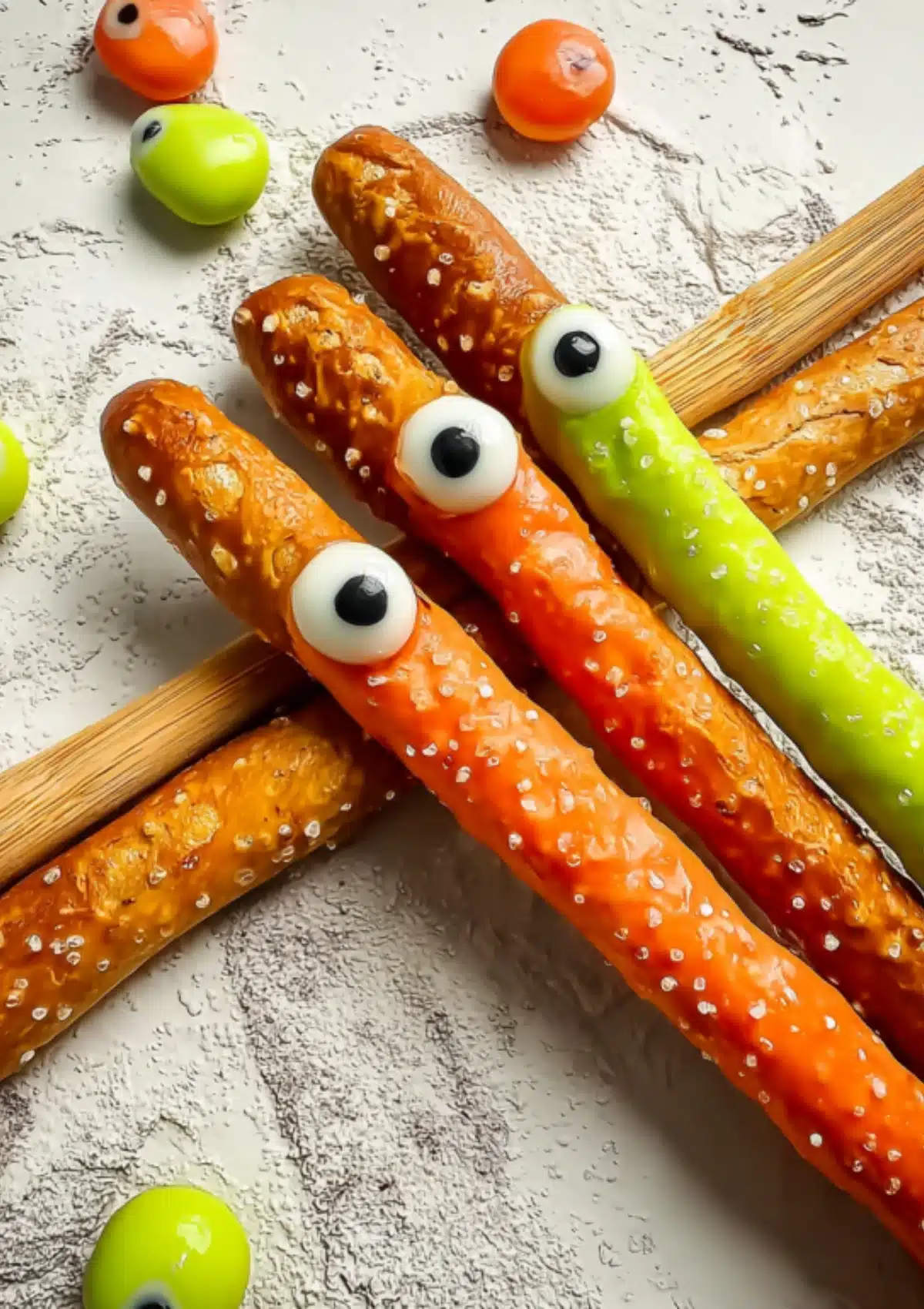 Close-up of Halloween monster pretzel rods with orange, red, and green chocolate coating and candy eyeballs on wooden surface