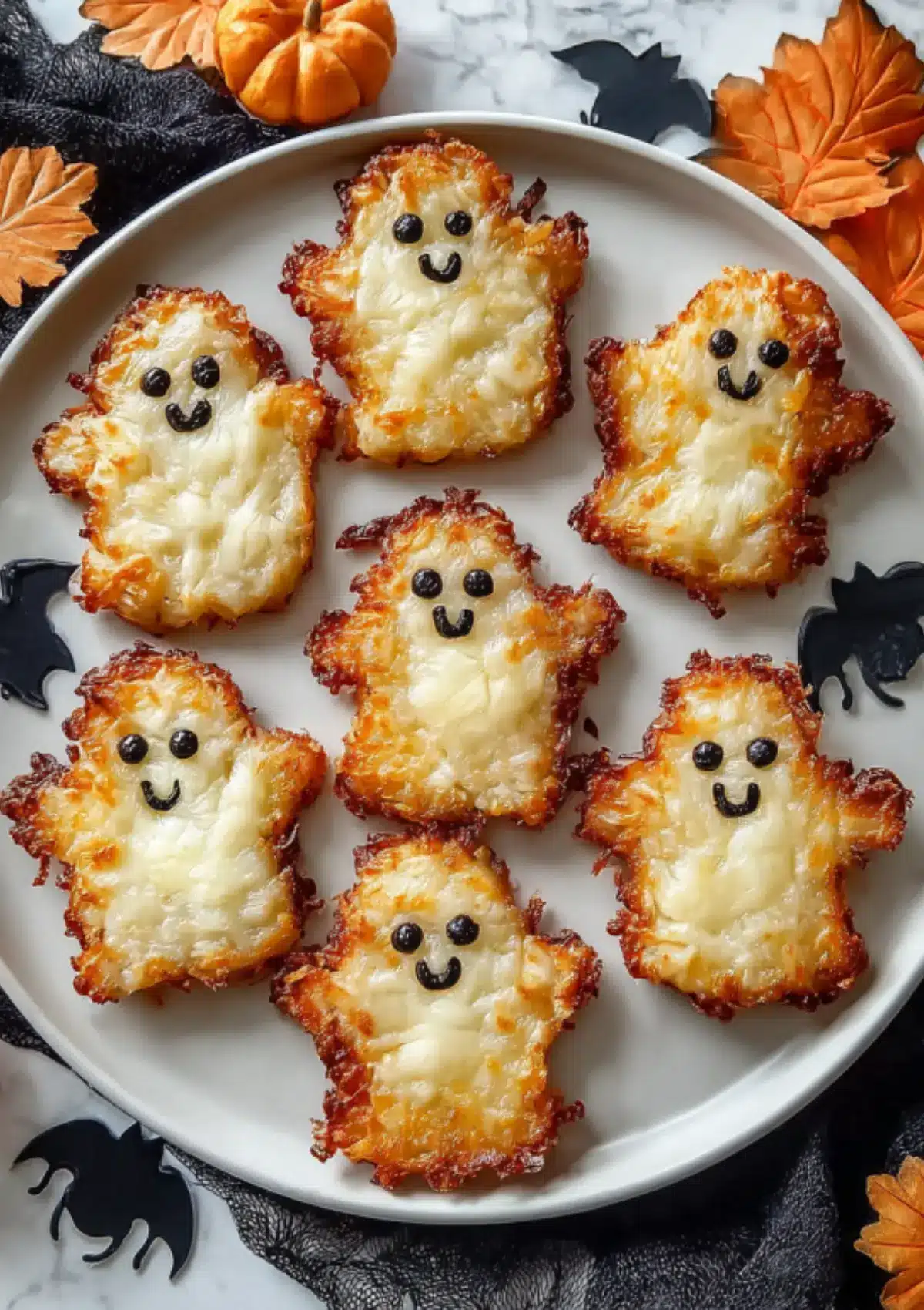 Close-up of spooky ghost hash browns with smiling faces made from black olives on Halloween-themed plate