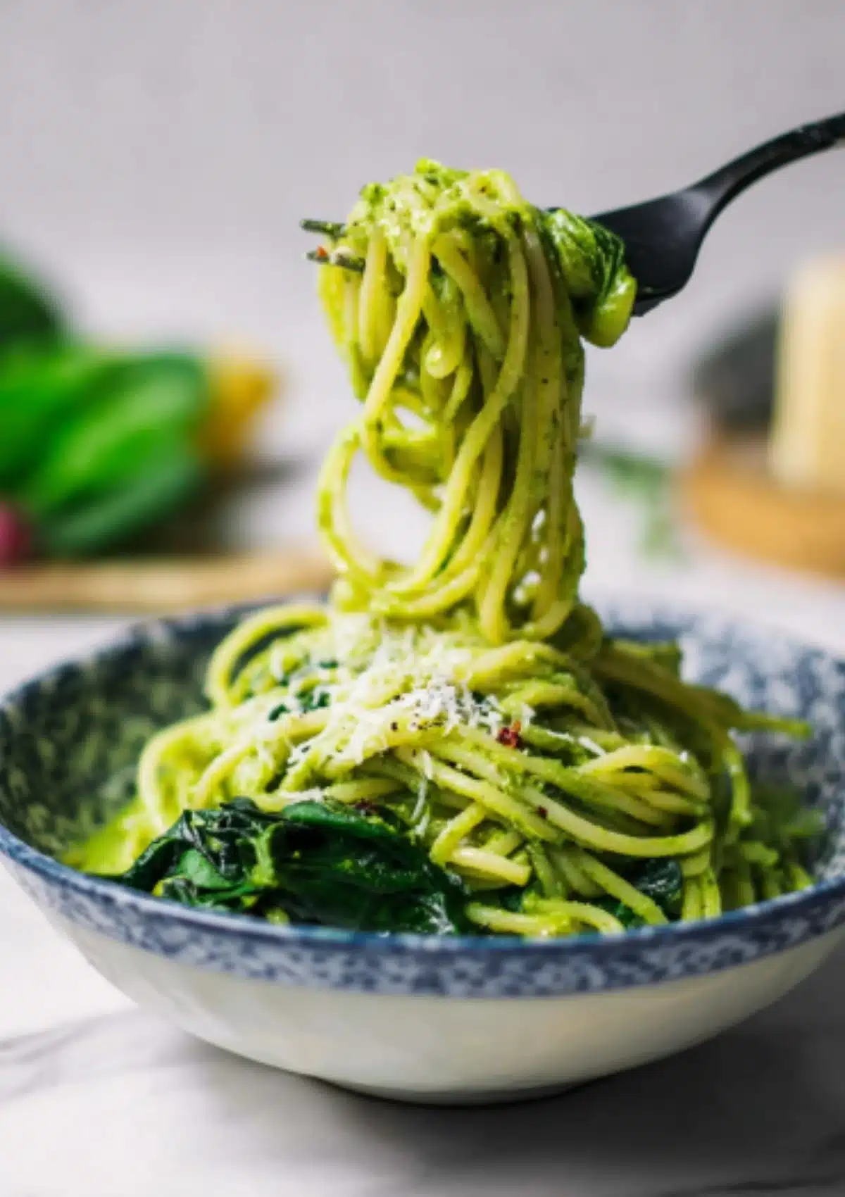 Fork twirling green pasta with spinach in a blue and white patterned bowl