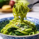 Fork twirling green spinach and pea pasta in blue patterned bowl