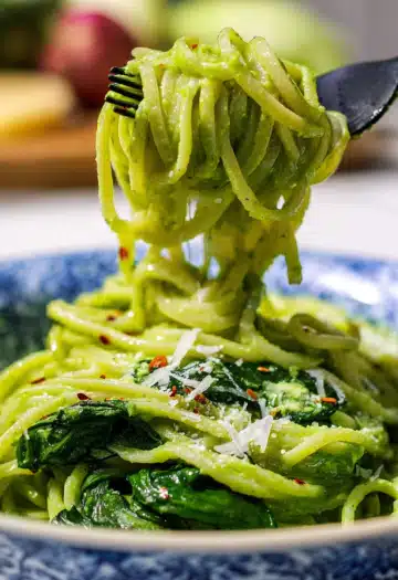Fork twirling green spinach and pea pasta in blue patterned bowl