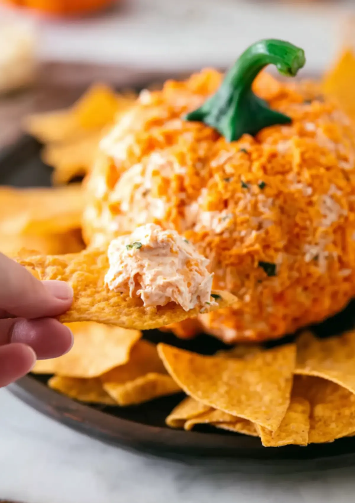 Hand dipping chip into pumpkin cheese ball