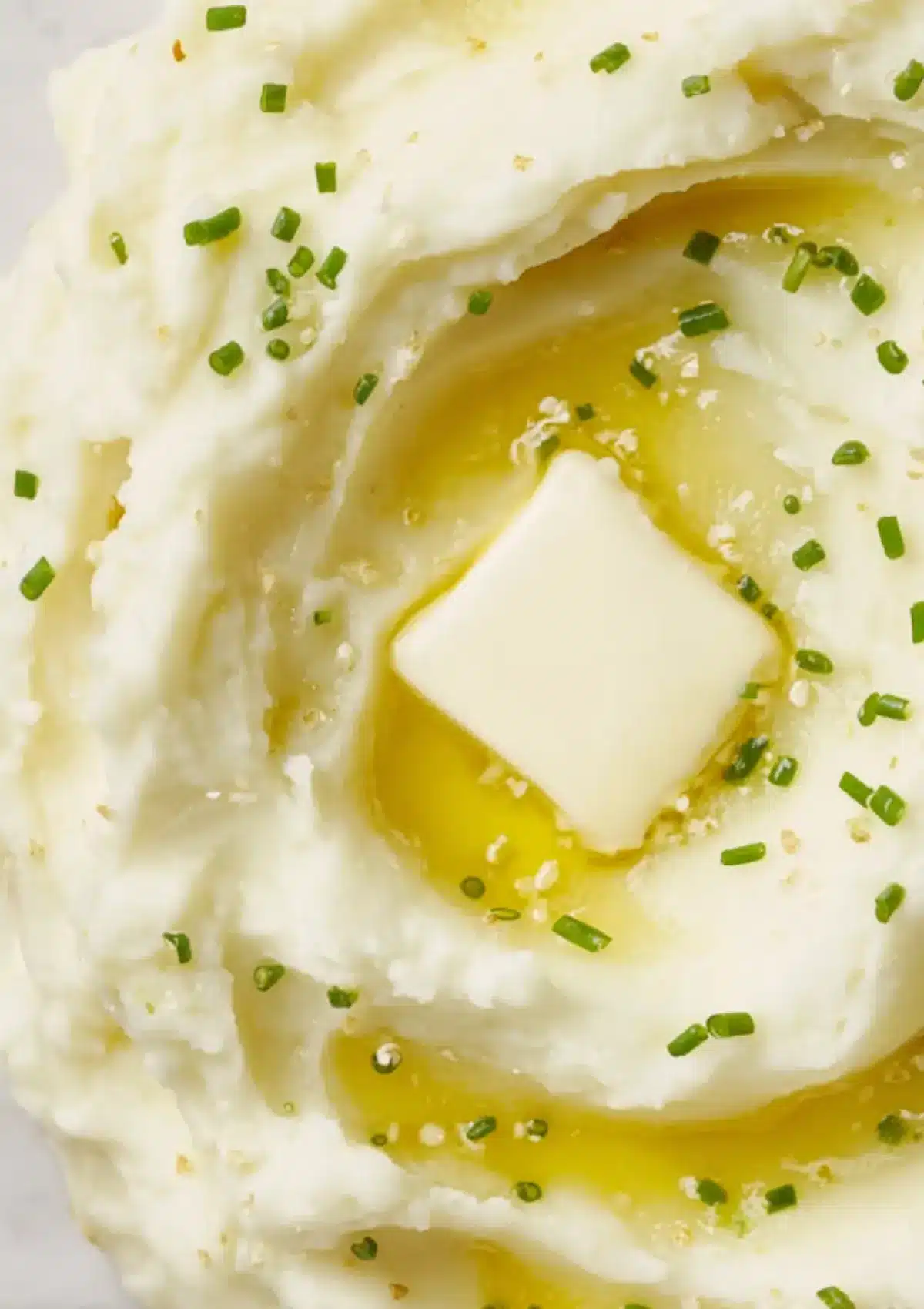 Butter melting into creamy mashed potatoes with chive garnish