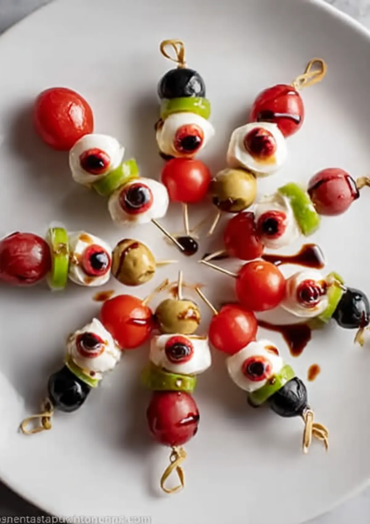 Caprese skewers arranged on white plate with mozzarella eyeballs