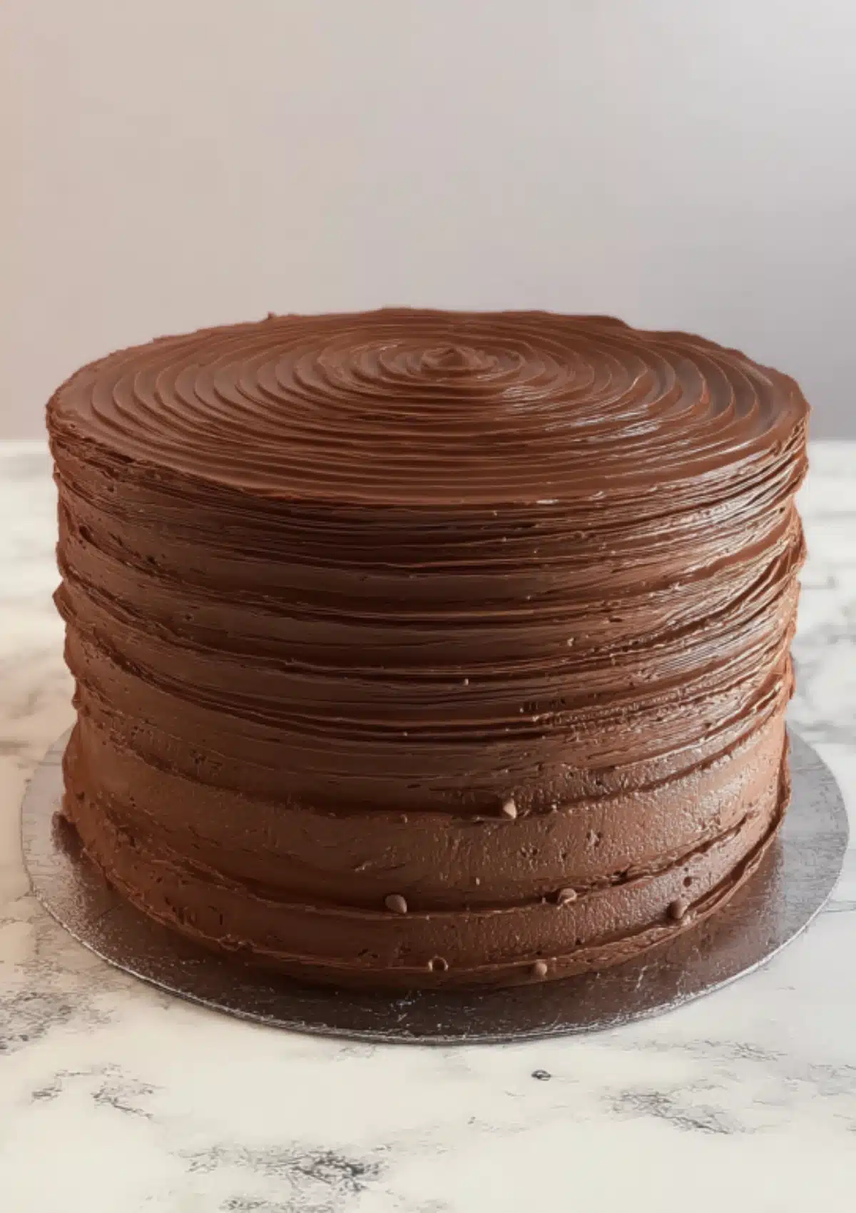 Chocolate layer cake with swirled frosting on silver cake board