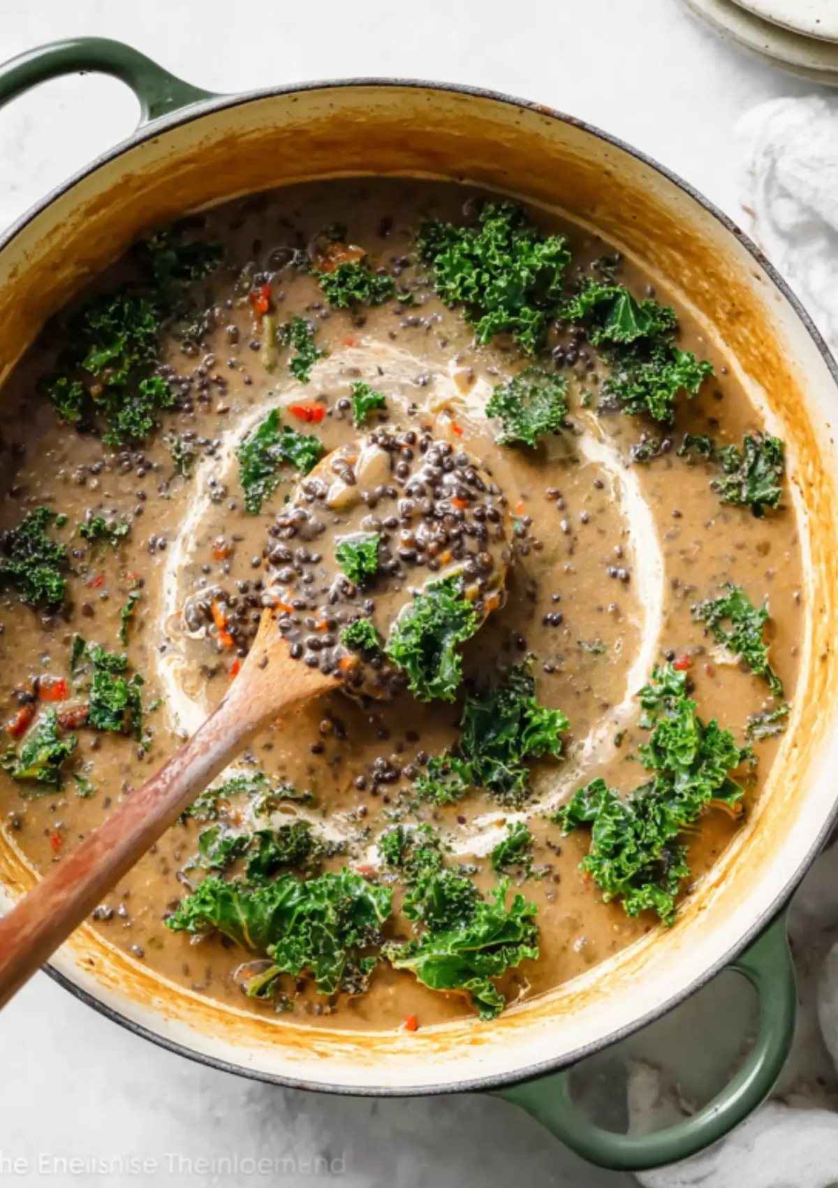 Coconut lentil soup in green Dutch oven with wooden spoon