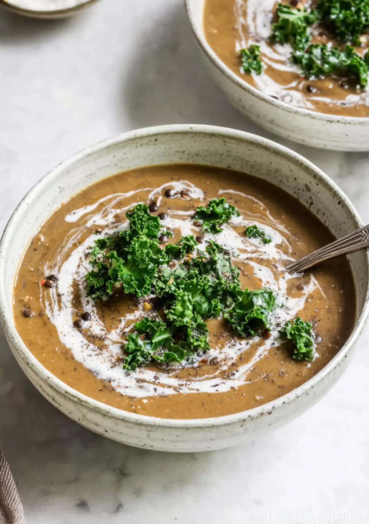 Creamy lentil soup in speckled bowl with kale and coconut cream swirl