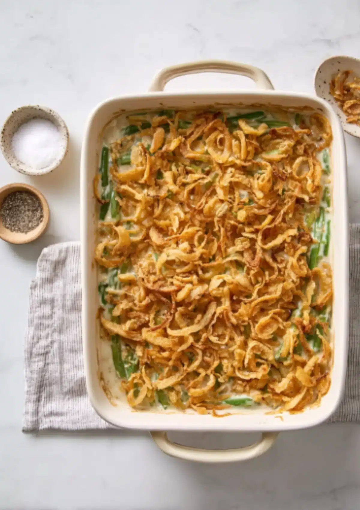 Green bean casserole with crispy fried onion topping in white baking dish