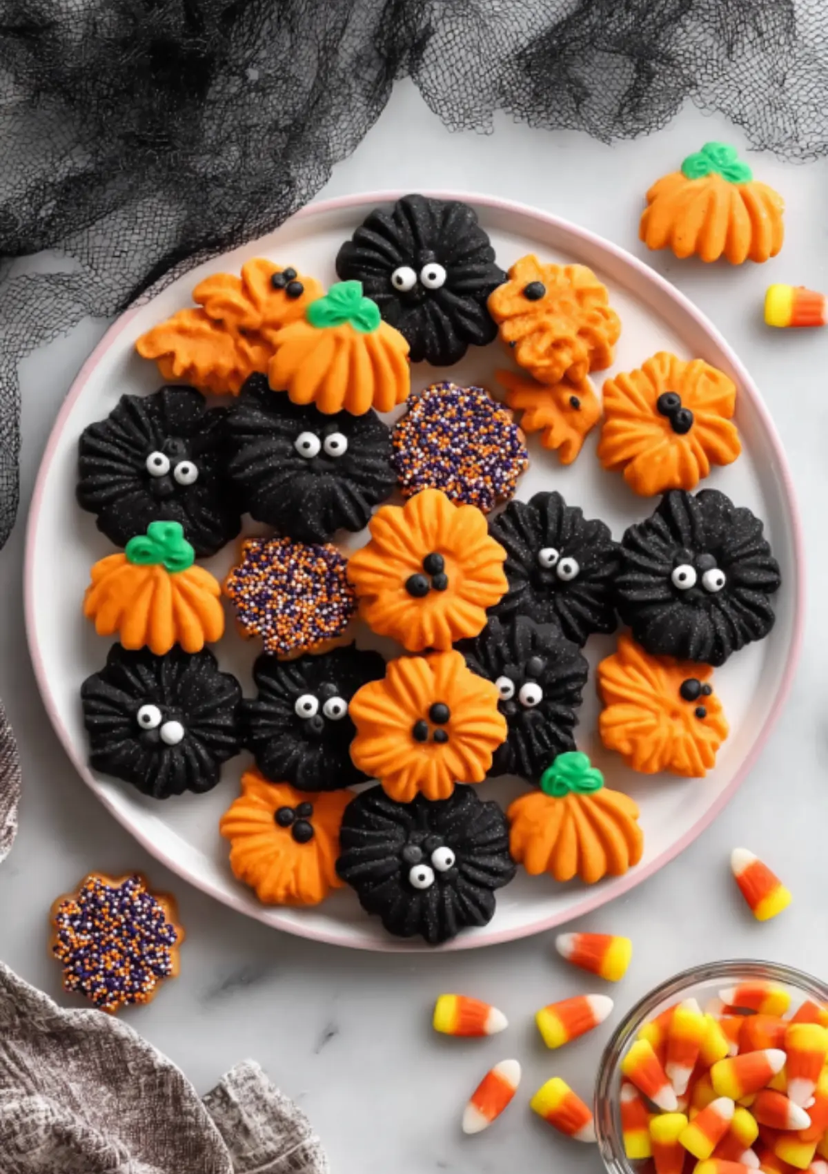 Halloween spritz cookies arranged on pink-rimmed plate with candy corn scattered around