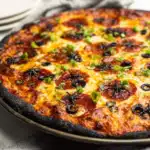 Side angle view of Halloween pizza with black crust on metal panSide angle view of Halloween pizza with black crust on metal pan