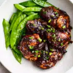 Soy sauce chicken thighs topped with scallions next to snap peas