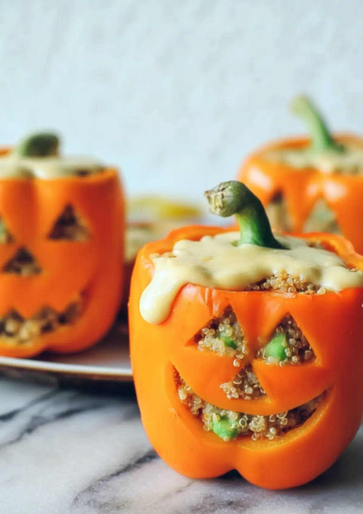 Three stuffed bell peppers with Halloween faces and white sauce on marble surface
