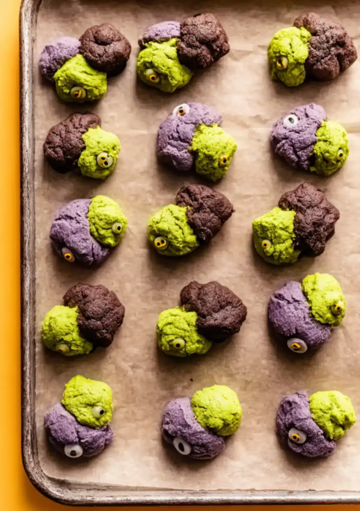Unbaked monster cookies on baking sheet with candy eyes