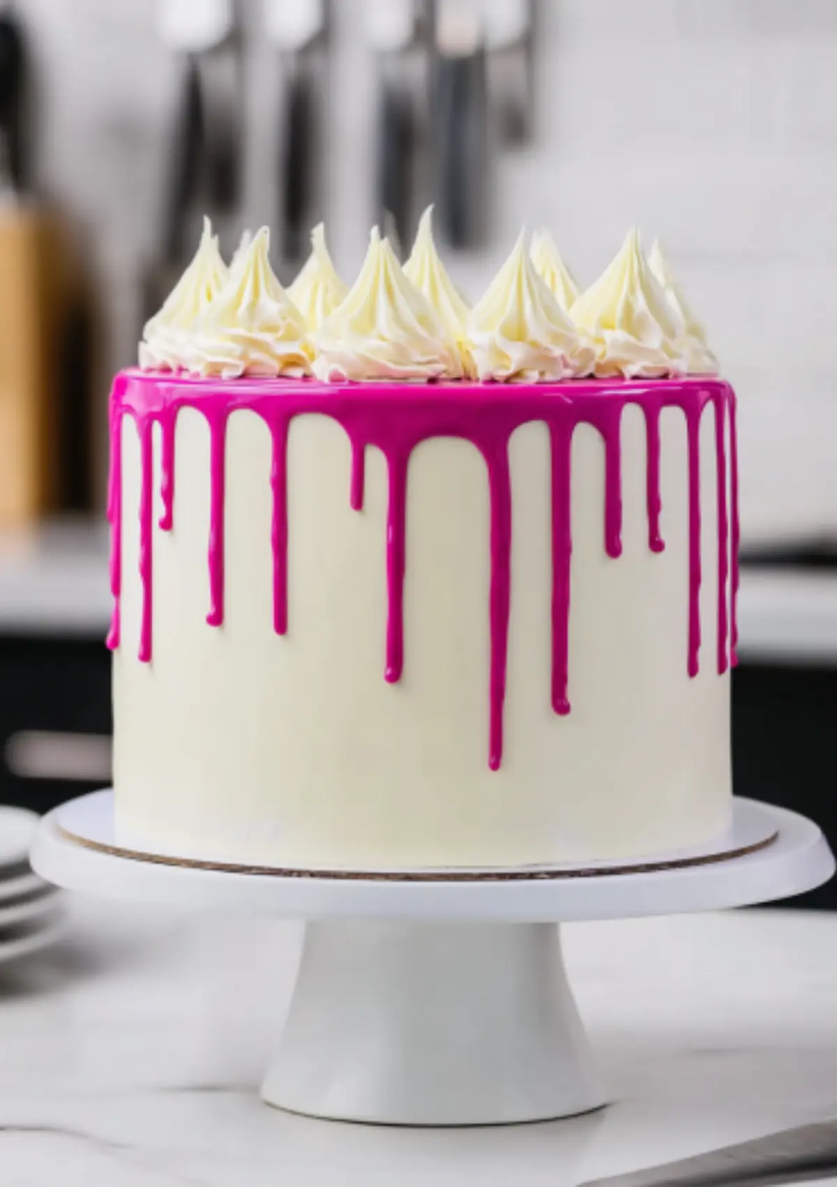 White frosted cake with pink drip and piped buttercream swirls on cake stand