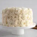 White rosette cake on pedestal with plates