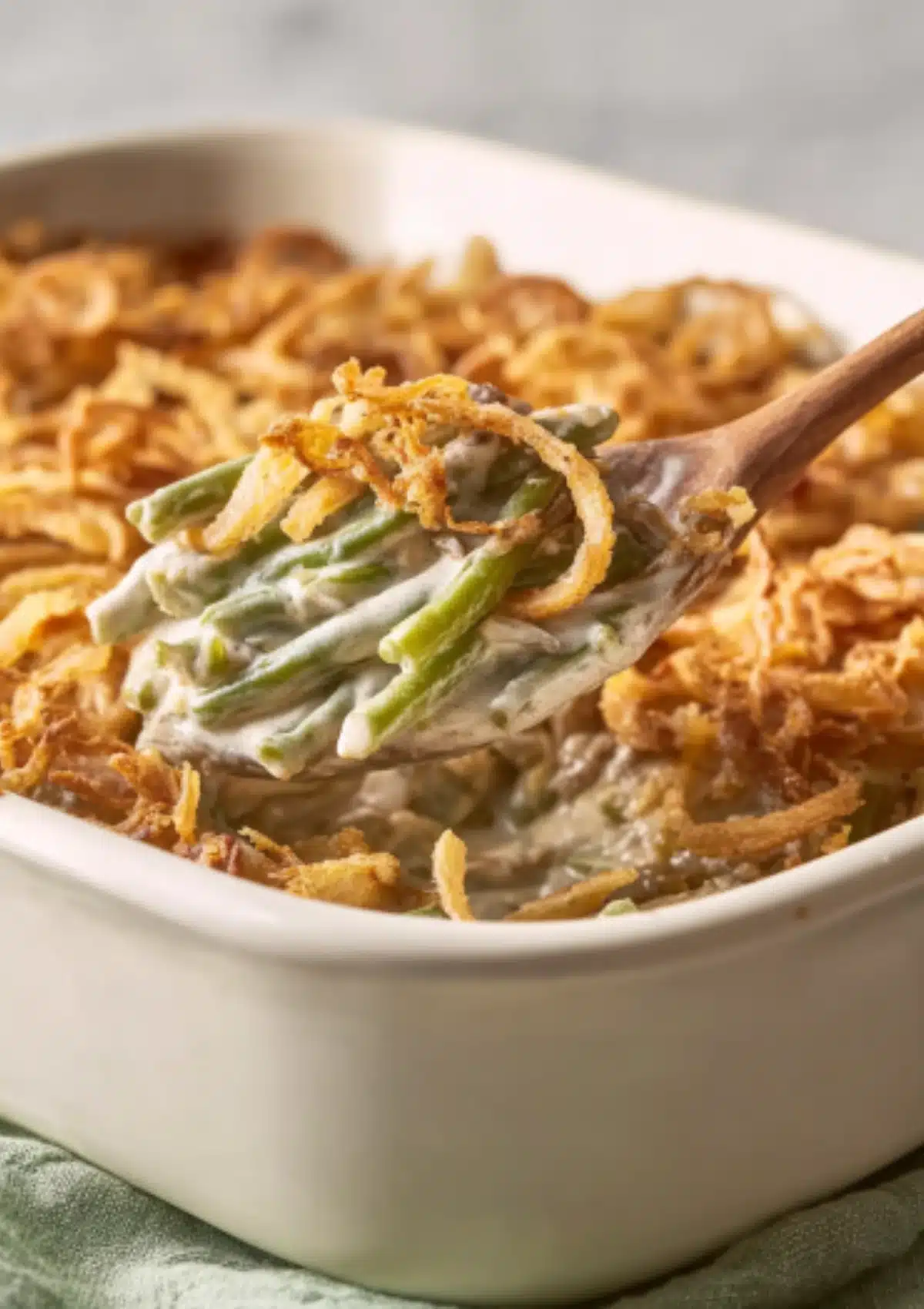 Wooden spoon lifting creamy green beans from casserole