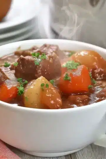 Best slow cooker beef stew recipe featuring tender beef cubes, carrots, and potatoes in rich homemade gravy, garnished with fresh parsley in white bowl