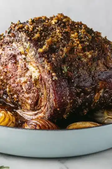 Golden-brown prime rib roast with roasted onions on white platter