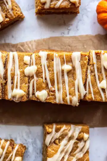 Row of pumpkin bars with white icing on parchment paper
