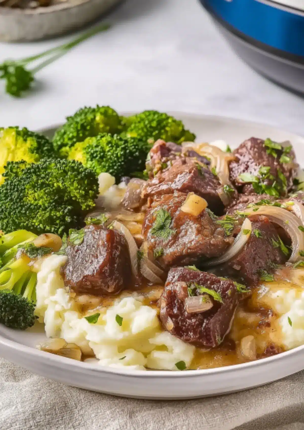 Detailed close-up shot of garlic butter steak bites with caramelized onions over fluffy mashed potatoes, accompanied by bright green steamed broccoli