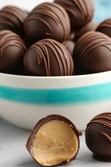 Chocolate covered peanut butter balls in turquoise and white striped bowl with one truffle cut in half showing smooth peanut butter center