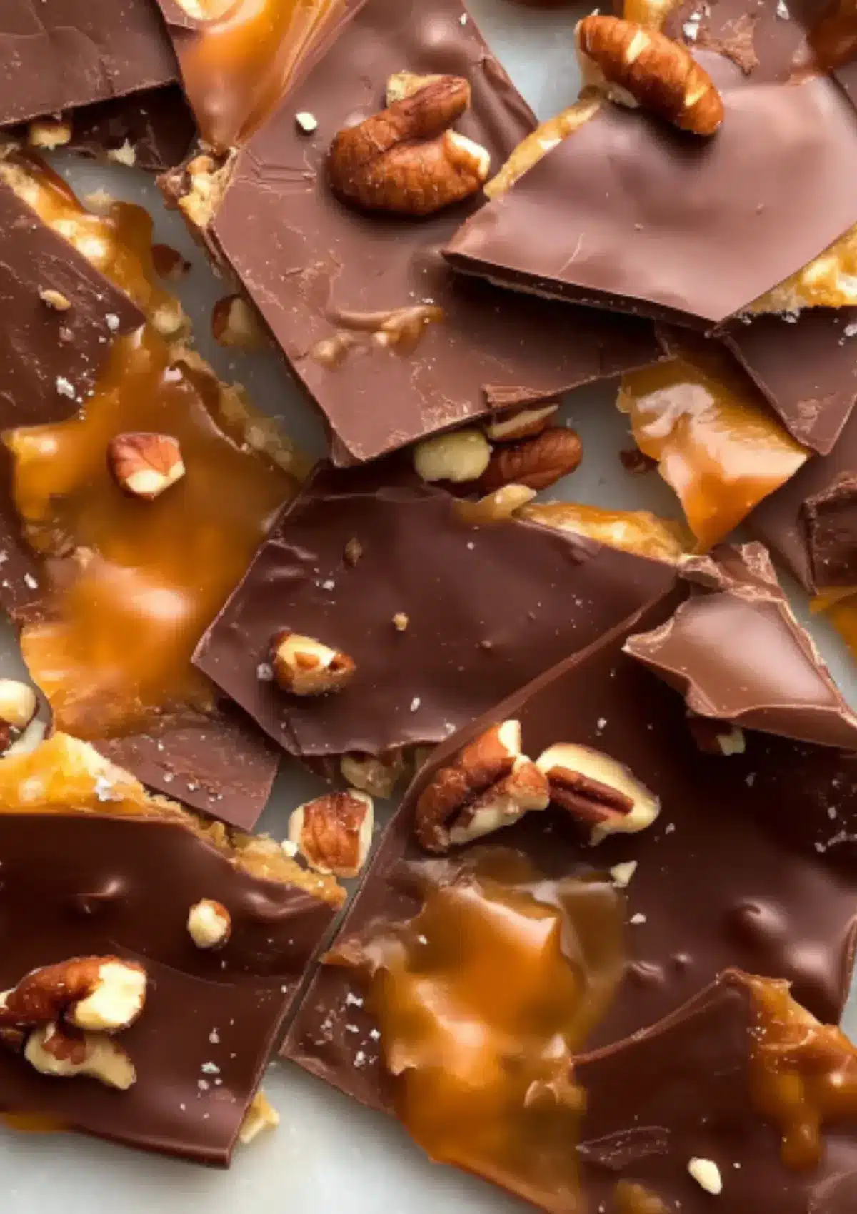Close-up of saltine cracker toffee pieces revealing layers of dark chocolate, buttery caramel, and embedded pecan pieces with glossy finish